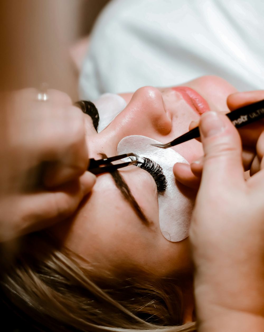An esthetician applying lash extensions with tweezers